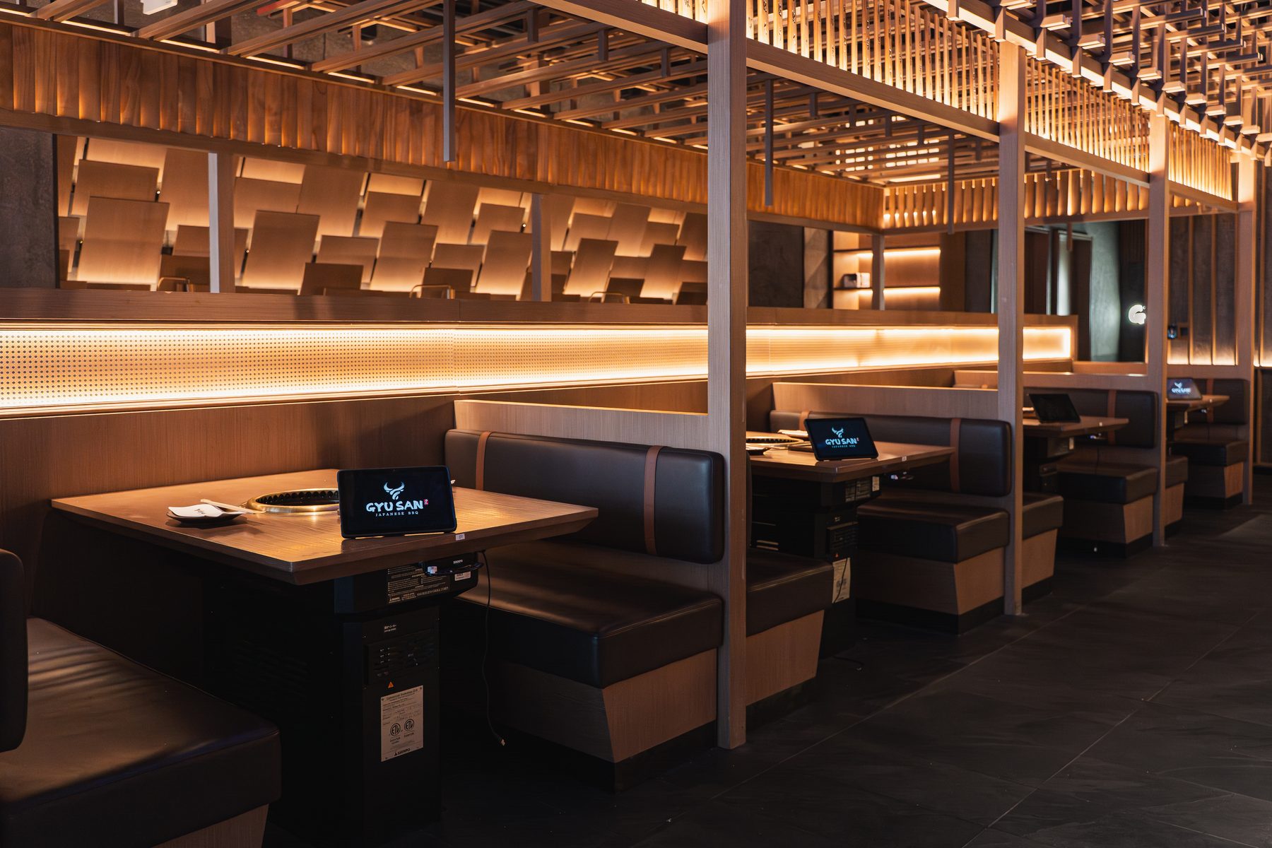 A row of dark leather booths with built-in grills under a lit wood-slat ceiling at Gyusan in Columbia