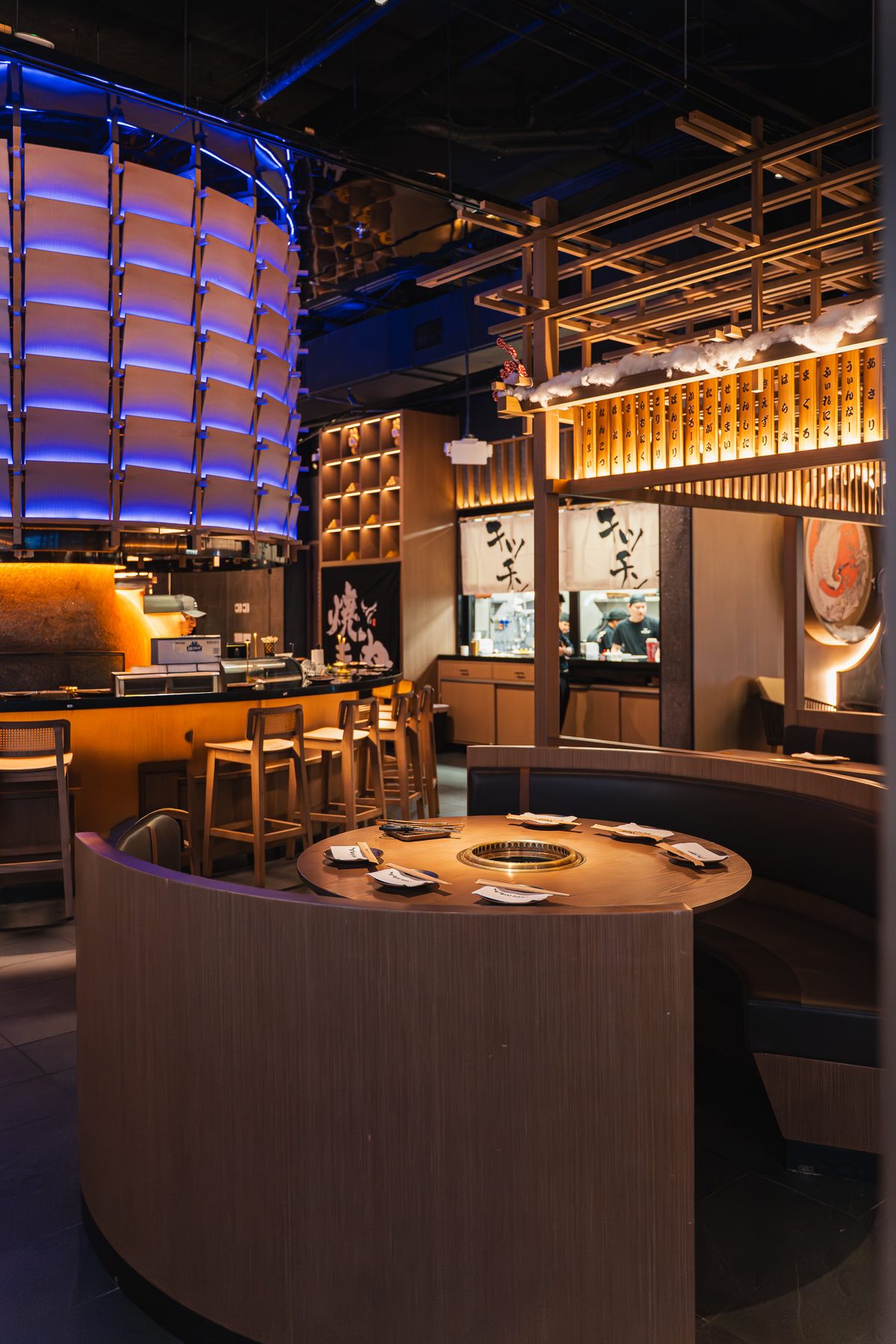 A curved booth around a round grill table, with the sushi bar's blue-lit canopy behind, at Gyusan Columbia