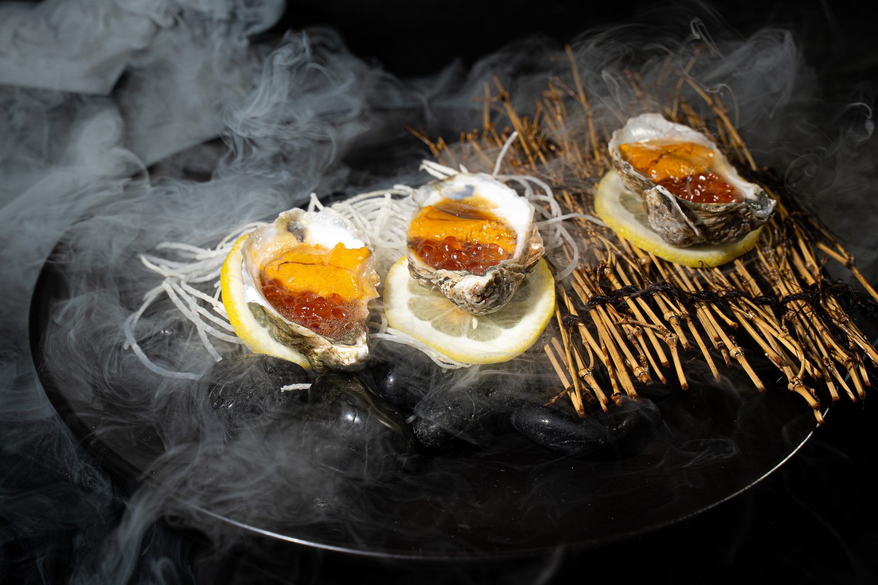 Three raw oysters topped with uni and ikura on lemon slices over dry-ice fog: Gyuzo's Oyster Tsunami