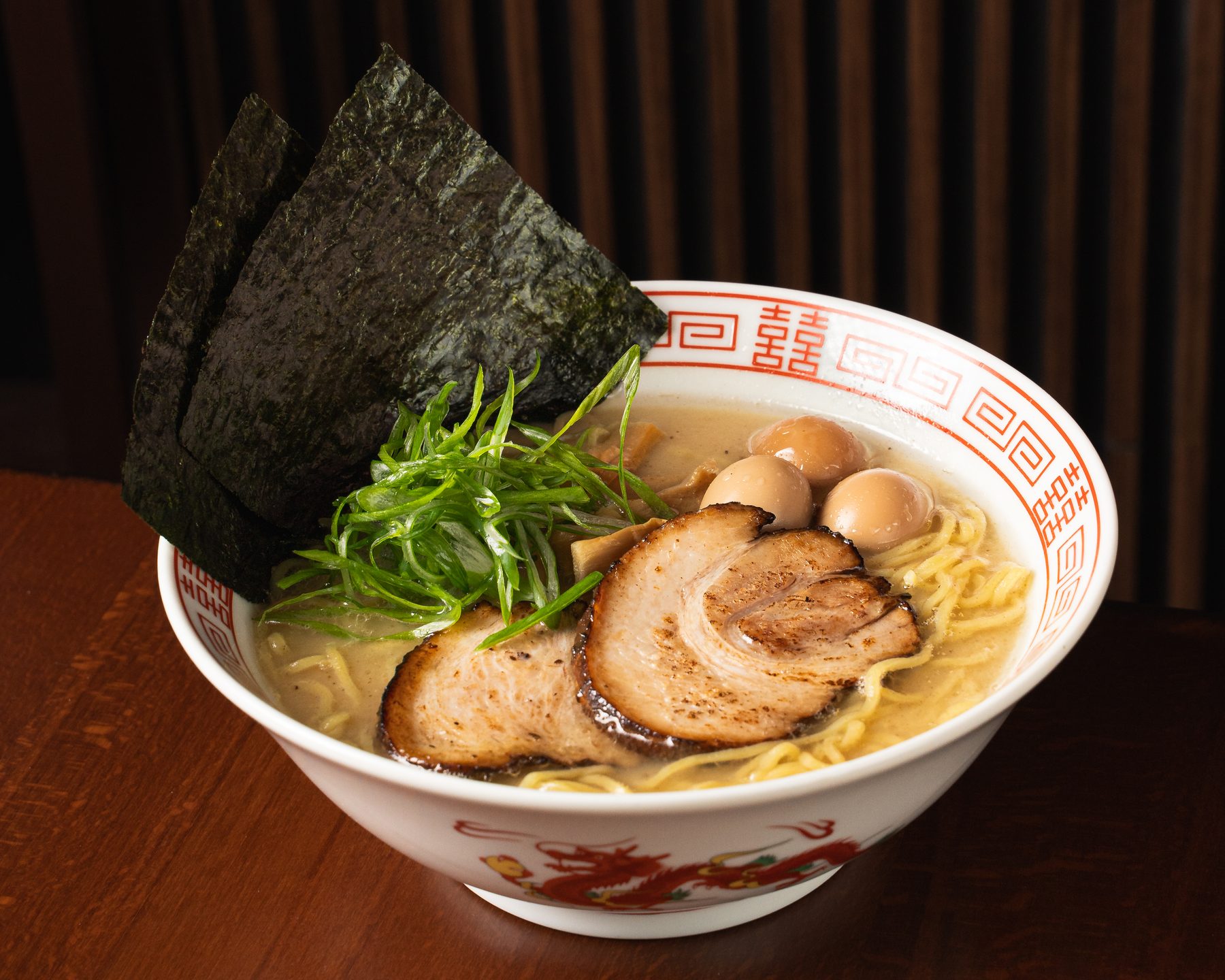 Tonkotsu ramen with chashu, quail eggs, scallions and two standing nori sheets in a white dragon bowl at Izakaya Nana