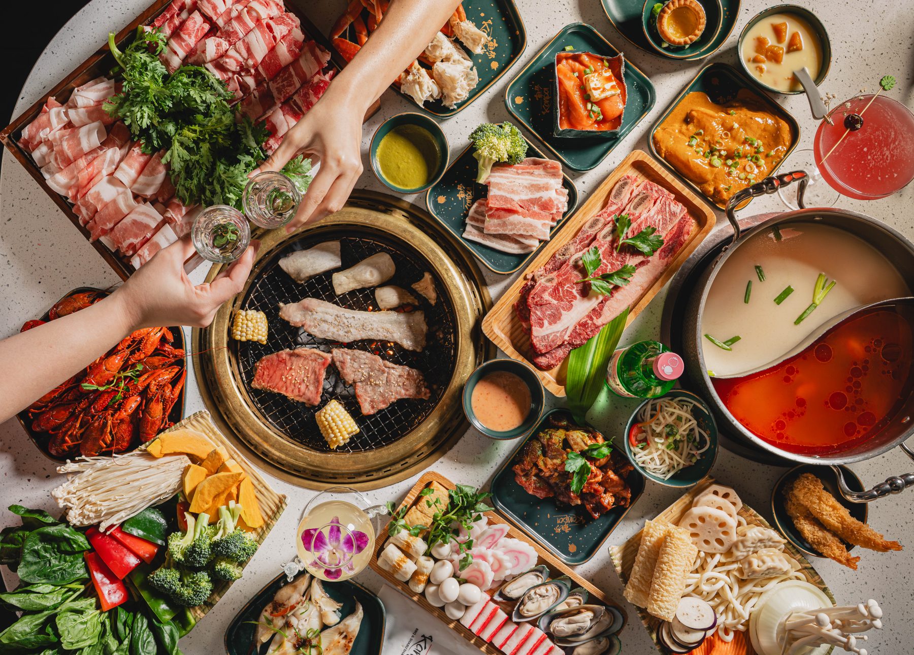 A spread of marinated meats, seafood and vegetables around the grill and a two-broth hot pot