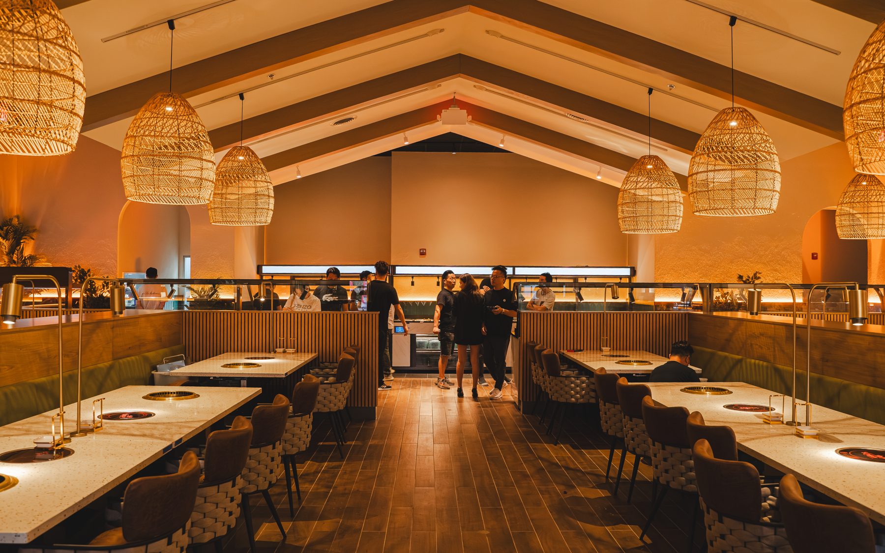 The dining room at Kanpai BBQ & Hotpot, with woven pendant lamps and built-in grill tables