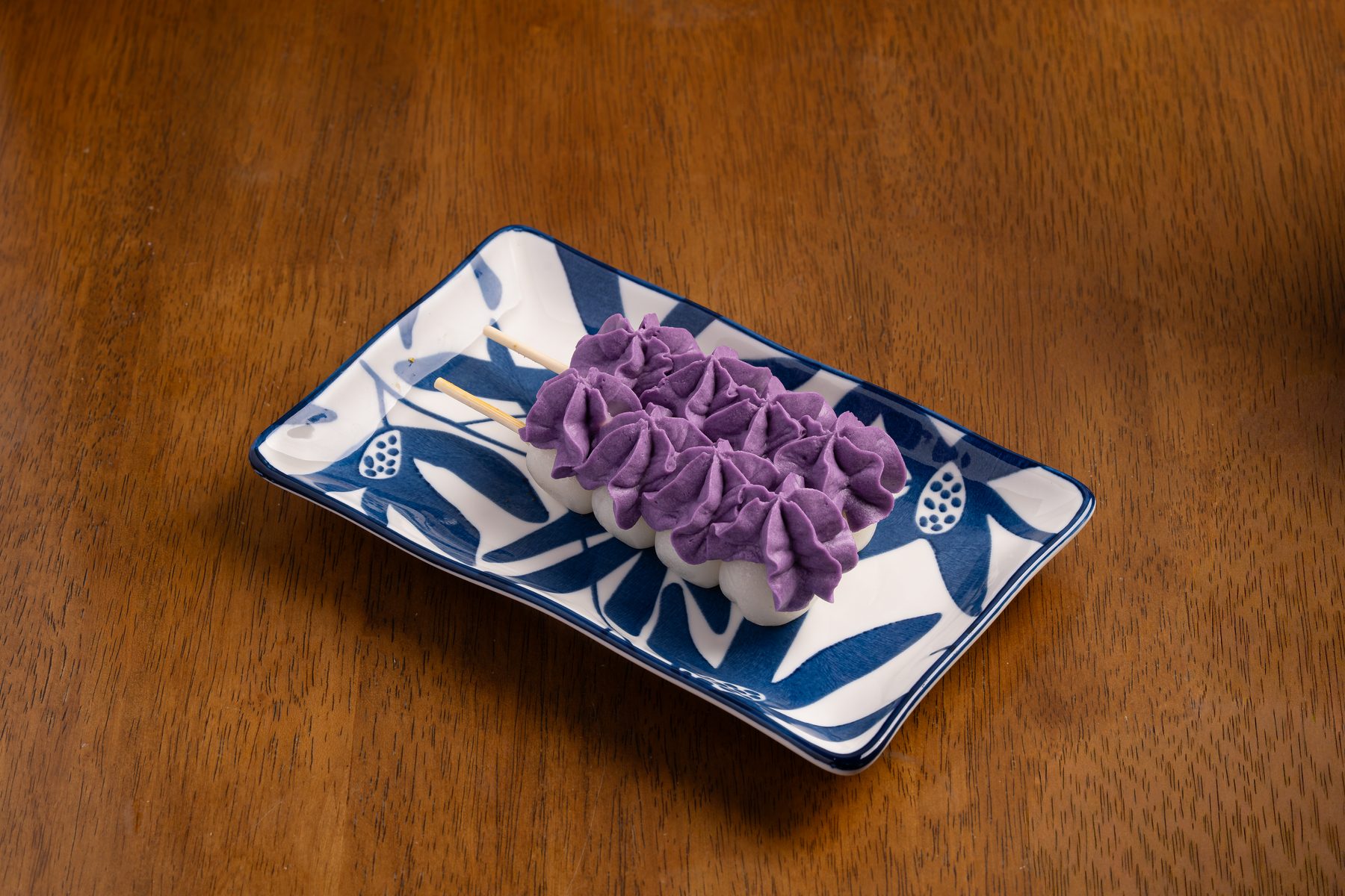 Two skewers of white dango topped with piped purple ube cream on a blue-and-white plate at Okaeri